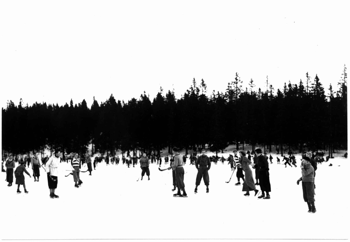 Tryvann skøytebane, 1934. Skøyteløpere i sving på isen. Noen med bandykøller. 