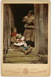 Samefamilie i døråpningen på et hus. Mann, kvinne og lite ba