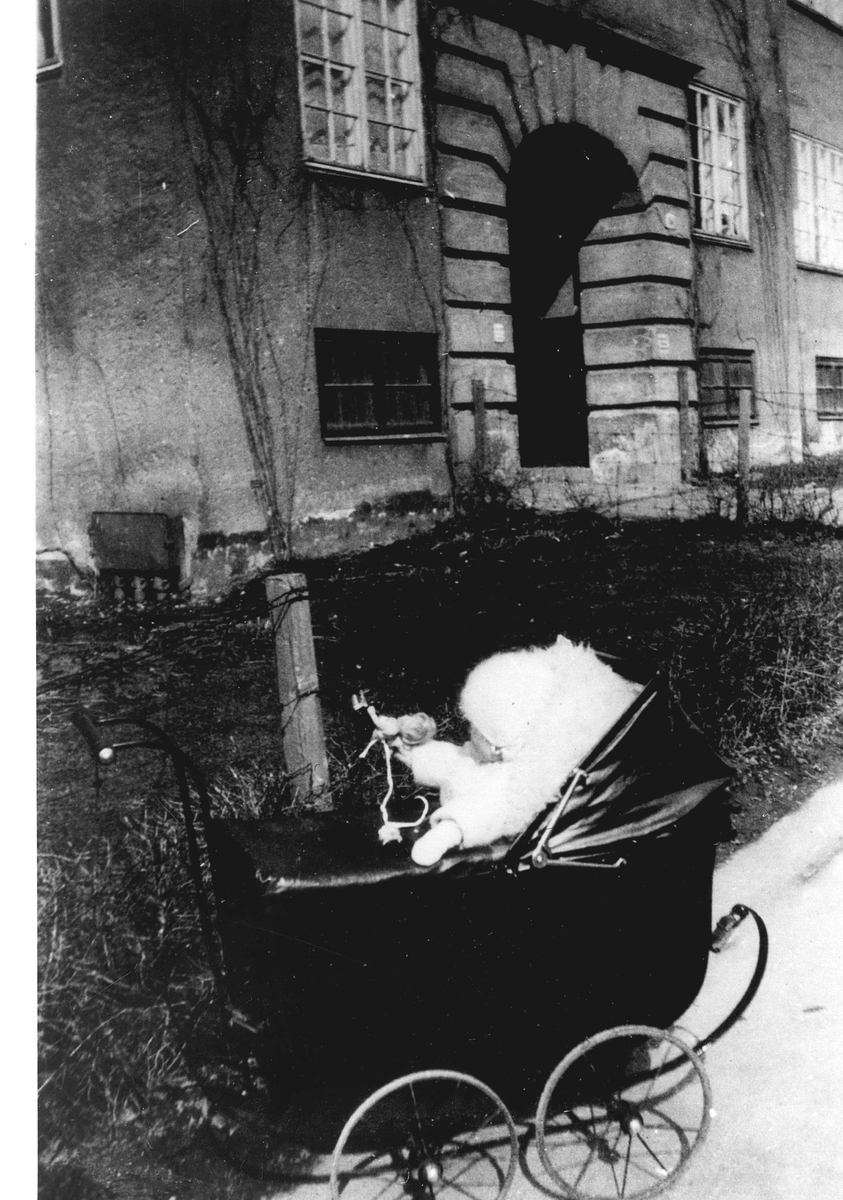 Barn i barnevogn foran bygård. Familiens datter Jorunn Fossberg i barnevogn foran sitt barndomshjem i Jacob Aalls gate 60, Oslo i 1928.
Fra Jorunn Fossbergs familiealbum.