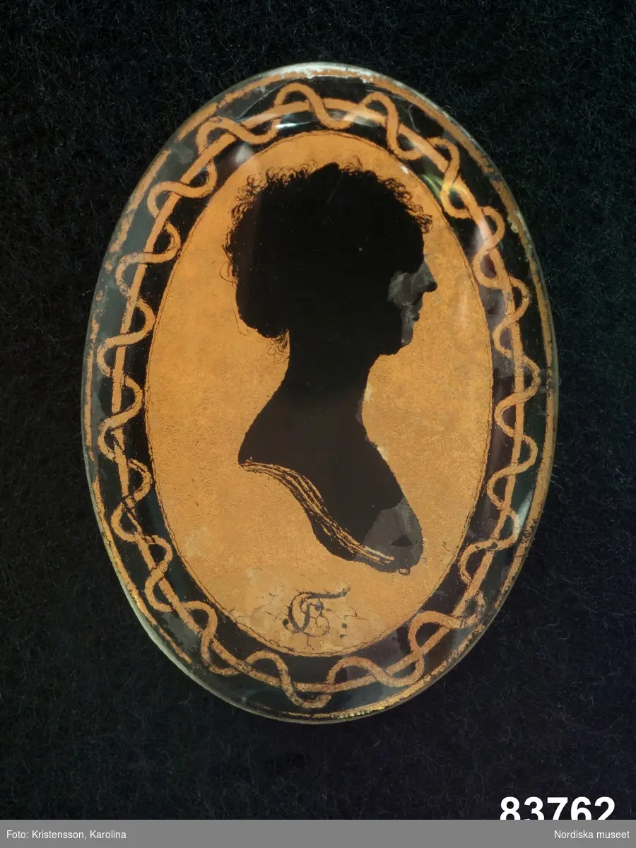 Silhuettporträtt, kvinna, bröstbild höger profil inom oval kantbård.