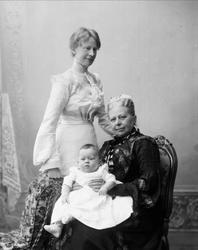 Gruppe, tre generasjoner kvinner. Kvinne i mørk kjole sitter