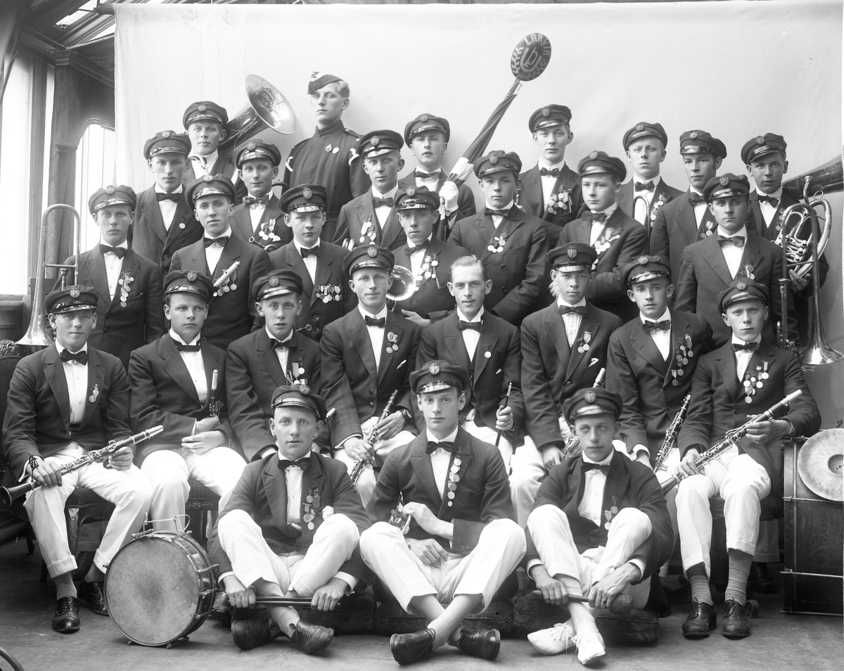 Gruppeportrett, Larvik guttemusikkkorps med instrumenter. Lyse bukser, mørk jakke og luer. Gardist i bakre rekke.