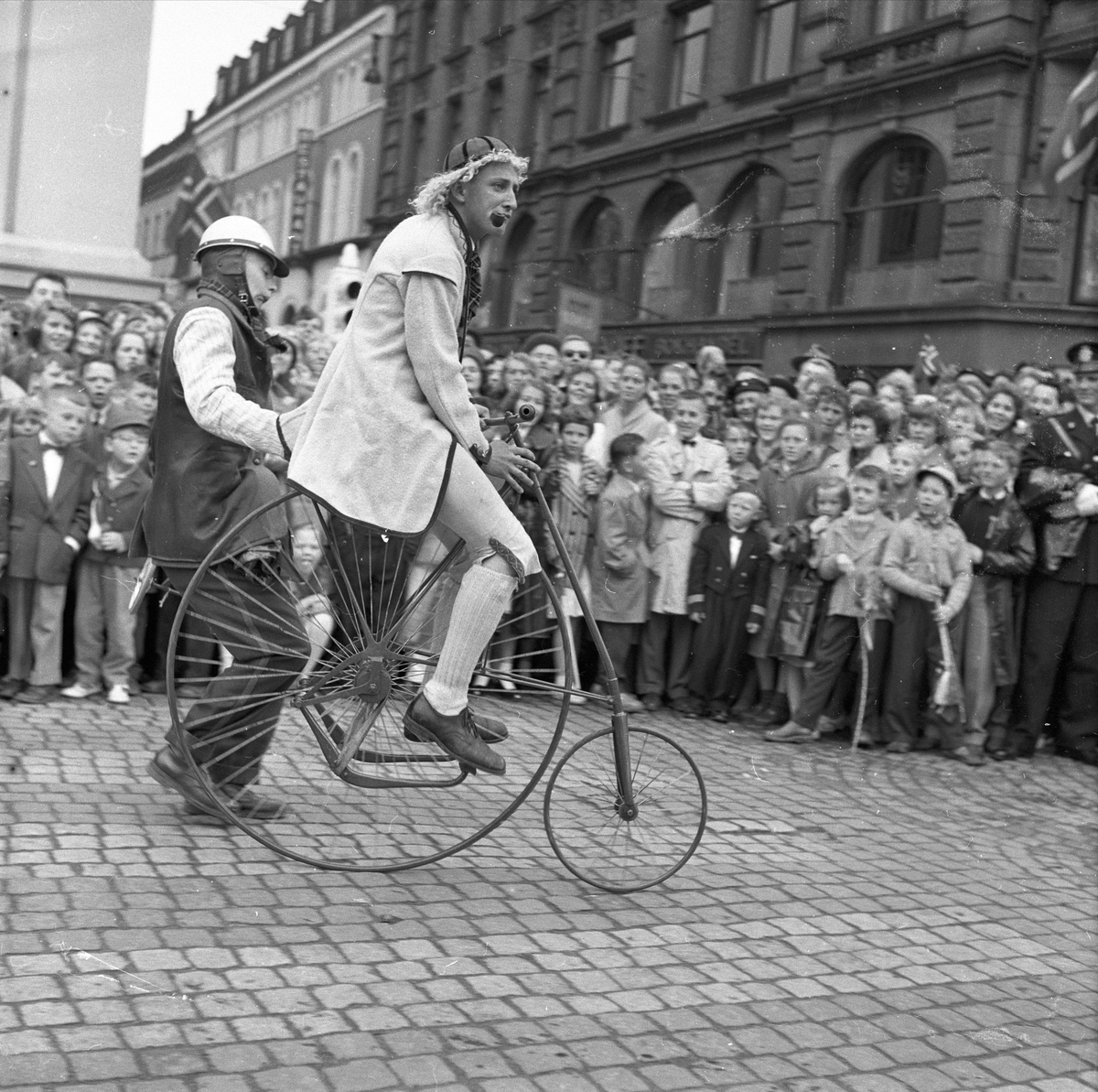 Karl Johans gate, Oslo, 17.05.1957. Rødrussens tog. Mann i bunad, sittende på en sykkel me lite hjul foran, stort bak.