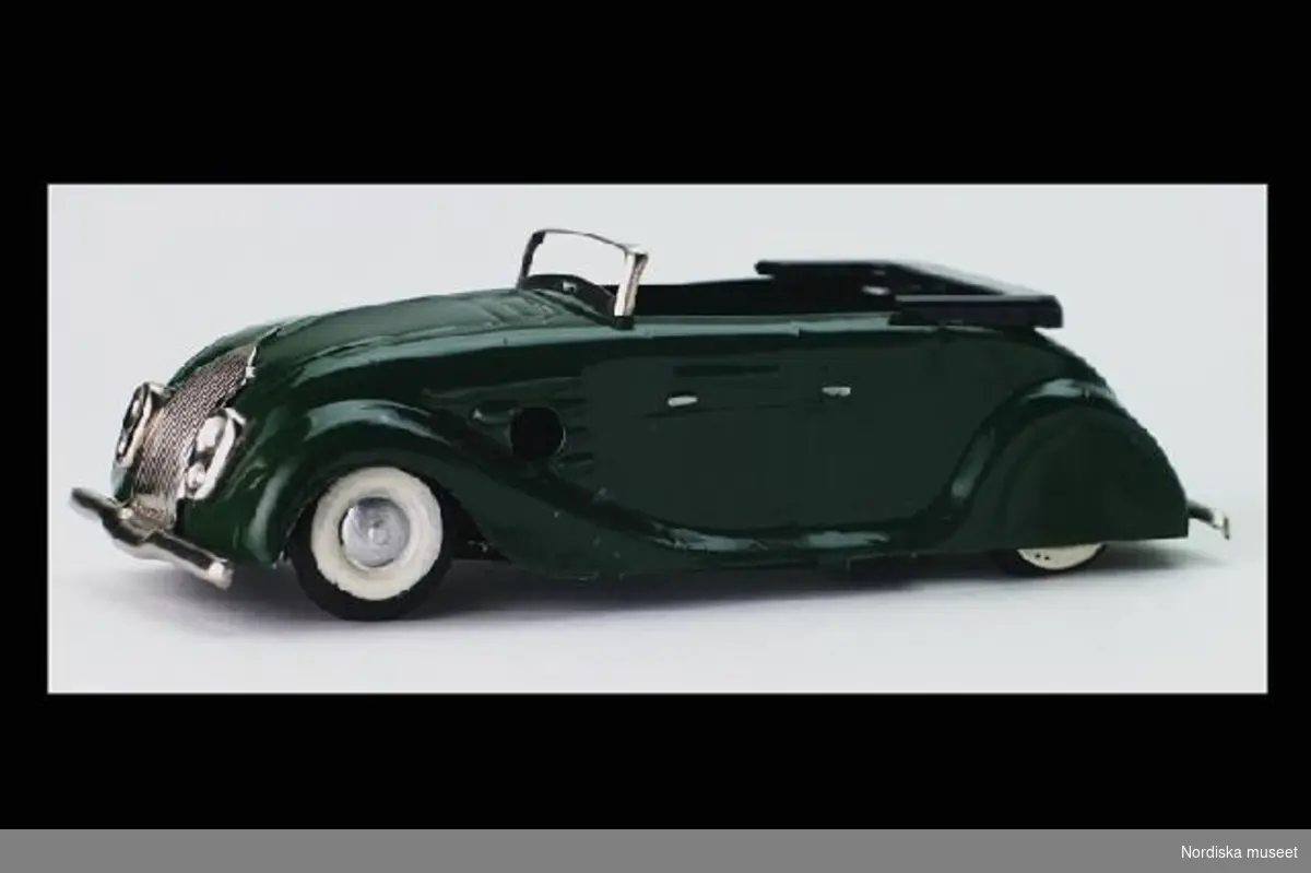 Inventering Sesam 1996-1999:
L 12,5 B 4,5 H 3 (cm)
Leksaksbil av grönlackerad plåt. Chrysler 1935 air flow cabriolet med nedfälld sufflett, karossen sammanfogad med metallflikar. Säten av trä, svarta gummidäck med vita däcksidor. 
Drivs med fjäderverk, nyckel saknas. 
Underredet märkt "TRI-ANG/ MINIC TOYS/ MADE IN ENGLAND". Enligt bilaga inköpt av givaren för 3,25 på Hagmans i Norrköping.
Bilen av modell "Chrysler Airflow Cabriolet 1935".
Bilaga
Birgitta Martinius 1996