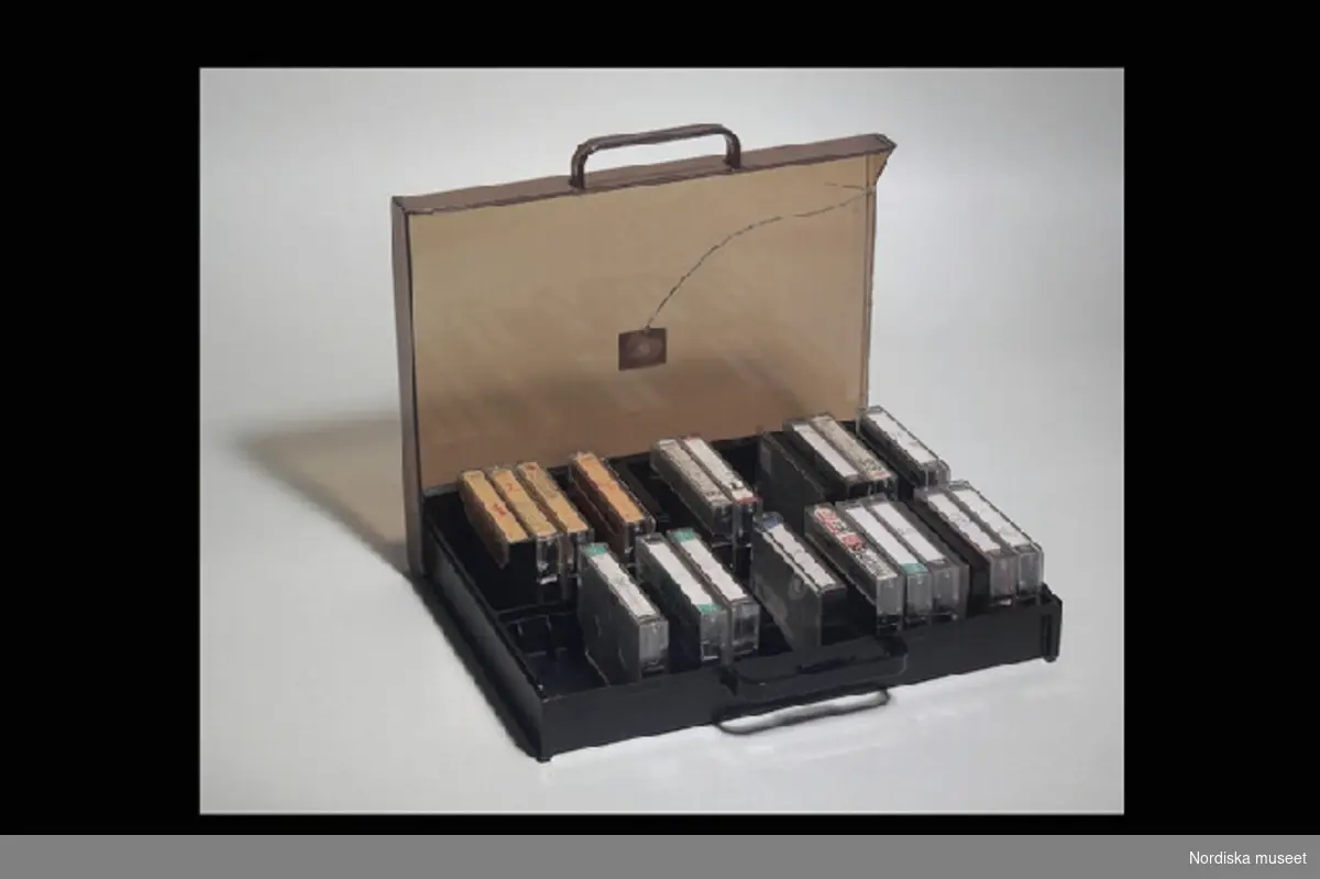 Inventering Sesam 1996-1999:
Kassettväska L 33 cm, B 25,5 cm, H 6 cm
Kassettband L 10 cm
Kassettbandsfodral L 11 cm
Kassettväska med kassettband.
Väska/lådan av brun hårdplast, transparent lock. Handtag. Under väskan etikett med text "Made in Hong Kong", på locket etikett "KASSETTVÄSKA". Locket har en spricka och gångjärnsfunktionen är trasig. väskan fack f¿r kassettband. I väskan finns 20 st kassettband, 18 st kassettbandsfodral av transparent plast (två med endast locket kvar) med omslag av papper, ett omslag ligger l¿st) På omslagen står det skrivet vilka dataspel som är inspelade på banden. Dataspelen är hemmakopierade på vanliga kassettband av märket Sony, Maxell (Japan), Philips (Beligien), AGFA (Tyskland)  och Basf (Tyskland).
Vid spel kopplades tangentbordet till en vanlig TV, en bandspelare, i vilken kassettbandet stoppades, och en transformator, ev även till joy stick.
Har brukats av Axel Brundin (f¿dd 1977) tillsammans med nedanstående f¿remål.
Dataspel och tillh¿rande f¿remål; Tangentbord ivn.nr 321.617 kasettbandspelare inv.nr 321.618, transformator inv.nr 321.619, Kasettväska med kassettband med olika dataspel inv.nr 321.620:1-24, tre joy sticks inv.nr 321.621 och 321.622, skokartong inv.nr 321.623 (i vilken kassettband f¿rvarades)  och Kassettband med spel 321.624-321.639
Instruktionsb¿cker, band- och kundf¿rteckning finns på arkivet.
Bilaga
EB 1995 [Elisabet Brundin]
Leif Wallin 1998