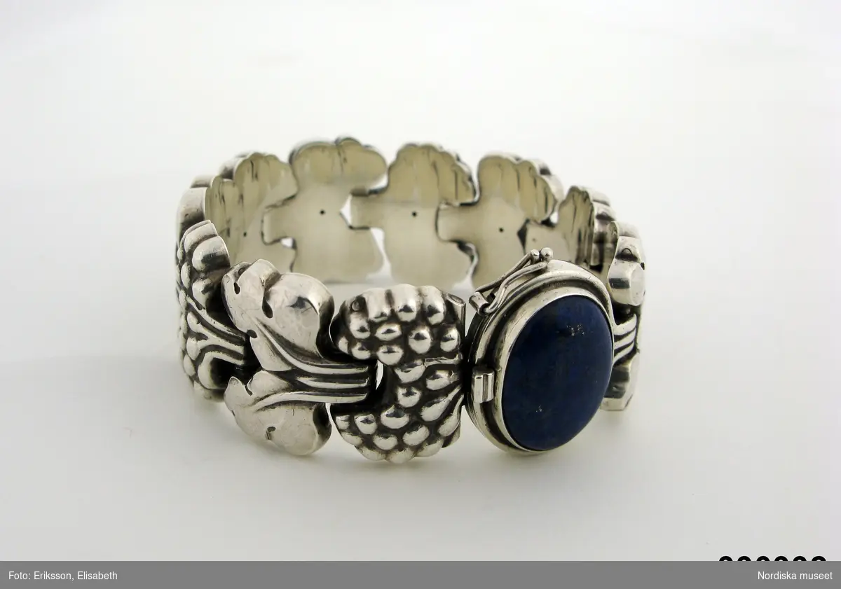 Armband, silver, bestående av 10 st kraftiga länkar med vinrankemönster. Fjäderlås  med oval dosa med oval, cabochonslipad lapiz lazuli-sten. Tillverkad hos Georg Jensen. Påskrift under låset: "Gunnel Dahlin Stockholm", samt 925 S, G, STERLING DENMARK, G,30, och därunder siffrorna 7673990 (ev ett telefonnummer) samt 1944.
Ingrid Roos 2010-08-23