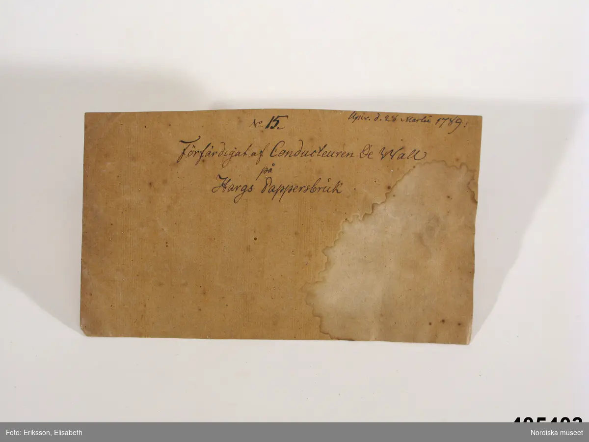 Pappersprov, kartong, en bit med text: "Upw. D. 28 Martii 1789" samt "No 15 Förfärdigat af Conducteuren De Wall på Hargs Pappersbruk".

Pappersprovet låg ursprungligen i ett brunt omslagspapper (ej förvärvat) tillsammans med färgningsprover (se inv.nr 405.402a-d). Omslagspapperet var hopvikt 340 x 220 cm, mycket söndrigt, med två små etiketter med handskrivet "No 23" och 2 större etiketter med text. På den vänstra: "Prof af Hargs pappersbruks tillwerkning år 1789. Af conducteur De Wall." och på den högra: " Prof på färgning med Svenska lafarter år 1803. Af Joh. P. Westman, Norrköping" (obs namnet Westring felskrivet)
/Elisabet Hidemark/
/Berit Eldvik 2008-03-25