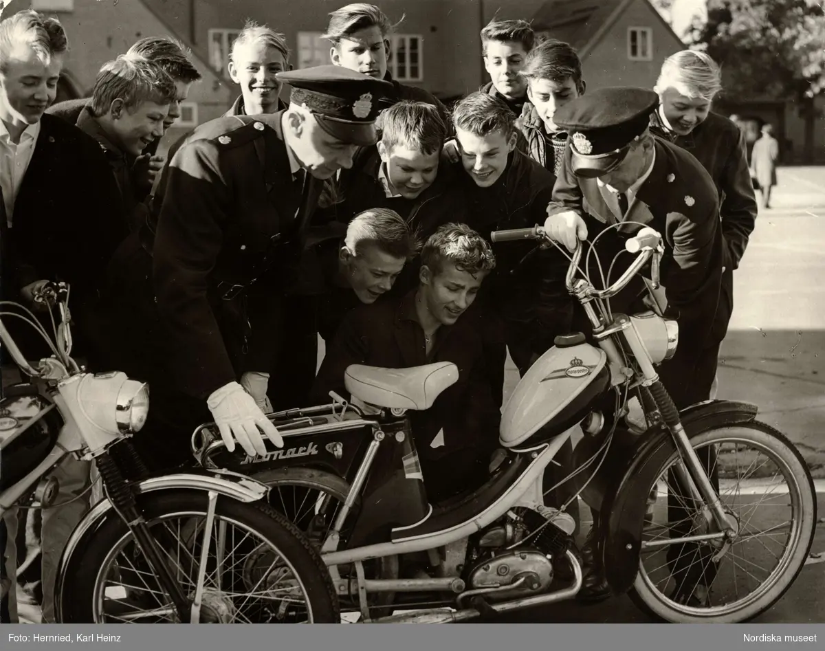 Polis i skola. Två polismän och en grupp pojkar undersöker en moped av märket Monark (monarpeden).