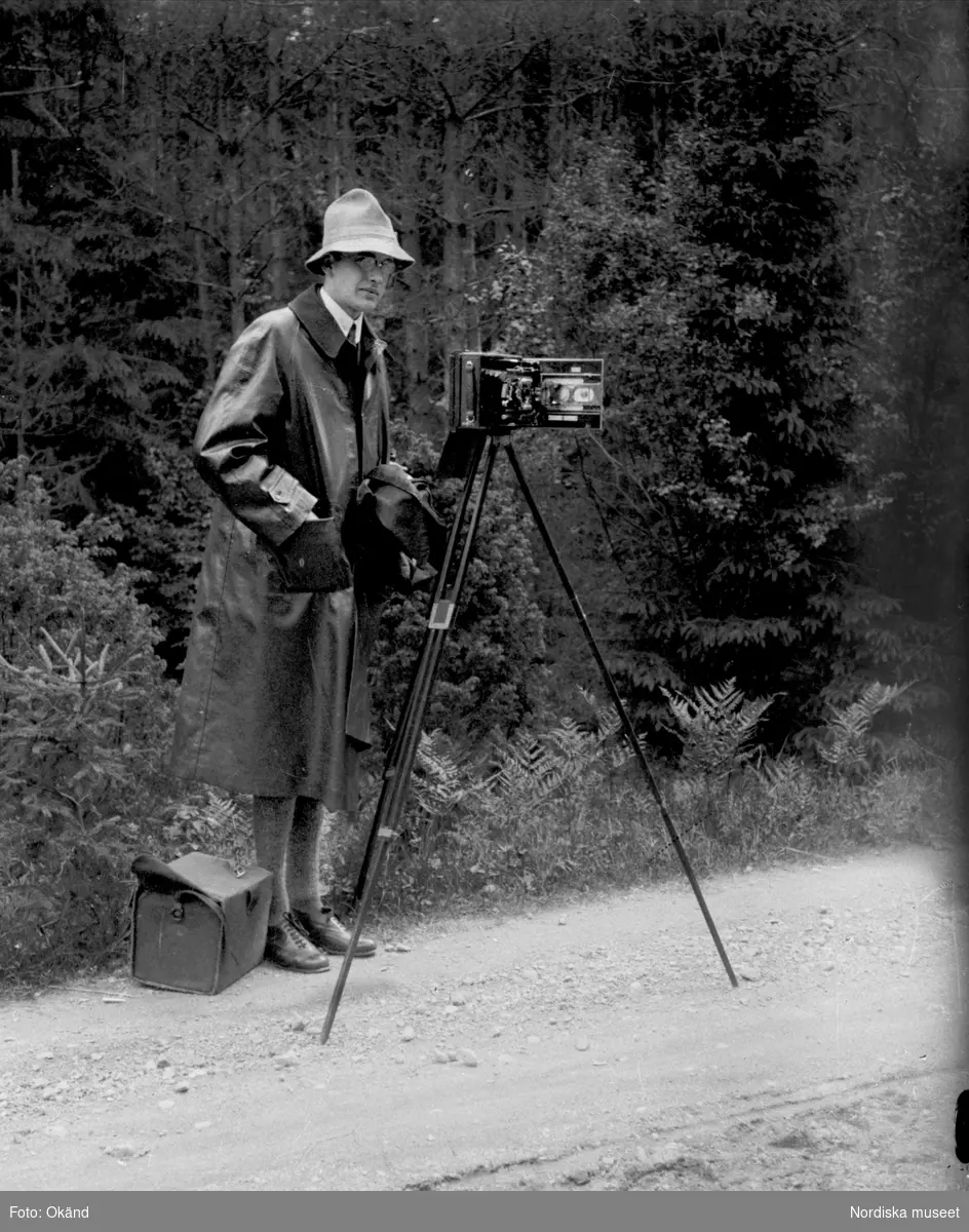 Gösta Berg, amanuens och senare styresman vid Nordiska museet, står vid en kamera monterad på stativ under en byundersökning i Dalarna
