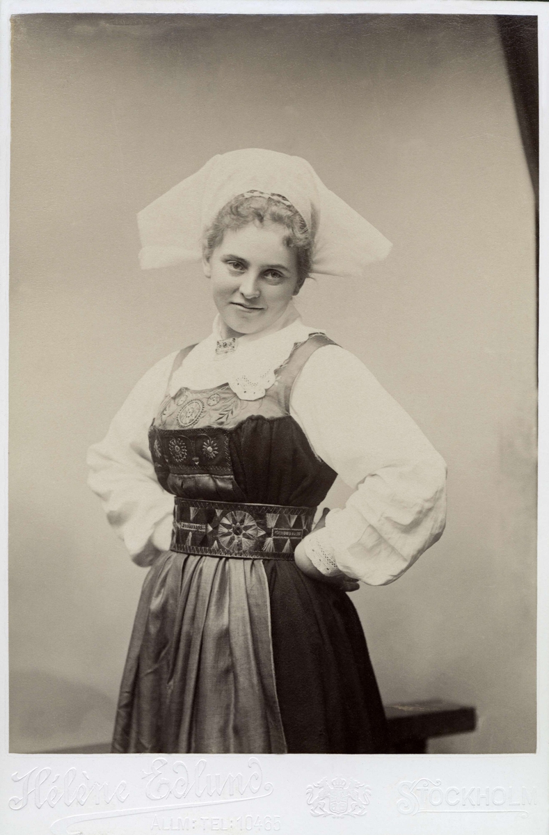 Porträtt på en kvinna i folkdräkt från Södermanland. Klädd i Österåkers högtidsdräkt, sydd troligen omkring 1900.