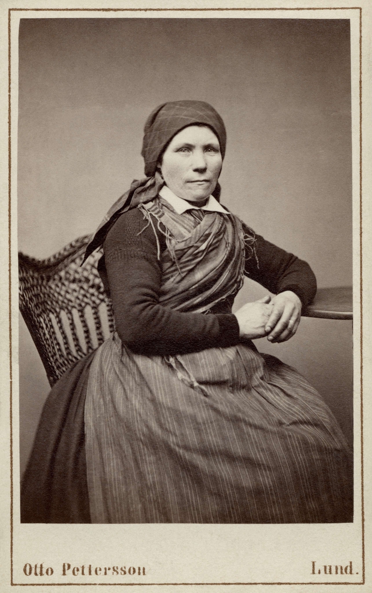 Kvinna poserar sittande i en sockendräkt, Löddeköpinge, Harjagers härad i Skåne. Inv. nr. 18518o.