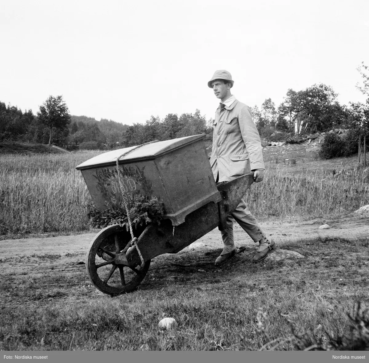 Torsten Lenk samlar föremål i Nösslinge socken, Halland i juni 1918. På en skottkärra kör han en fastspänd, målad brudkista.