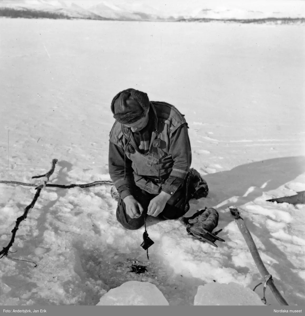 Fiske, Tjuonajokk, Gällivare socken, Lappland. Påskrift på monteringen:  "Andreas Labba tar upp nät, som han lagt under isen på Kattumälven. Ingen fångst."