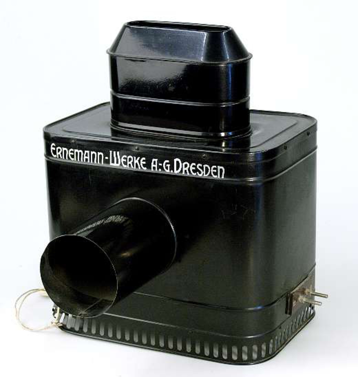 Skioptikonapparat av svart plåt. Text i guldfärg: ERNEMANN - WERKE A.-G. DRESDEN. Bildkassett på apparatens baksida. Projektionsrör (längd 11,5 cm) på framsidan. Två glödlampsfästen inuti apparaten. Apparaten är inte komplett.