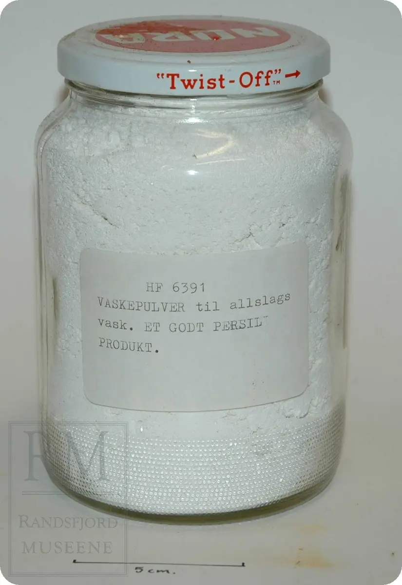 Form orginalembalasje: Avlang pappeske, hvit, blå, rød.
Nå: hvitt pulver på glass. Pulver tatt over på glass 23/11-1983