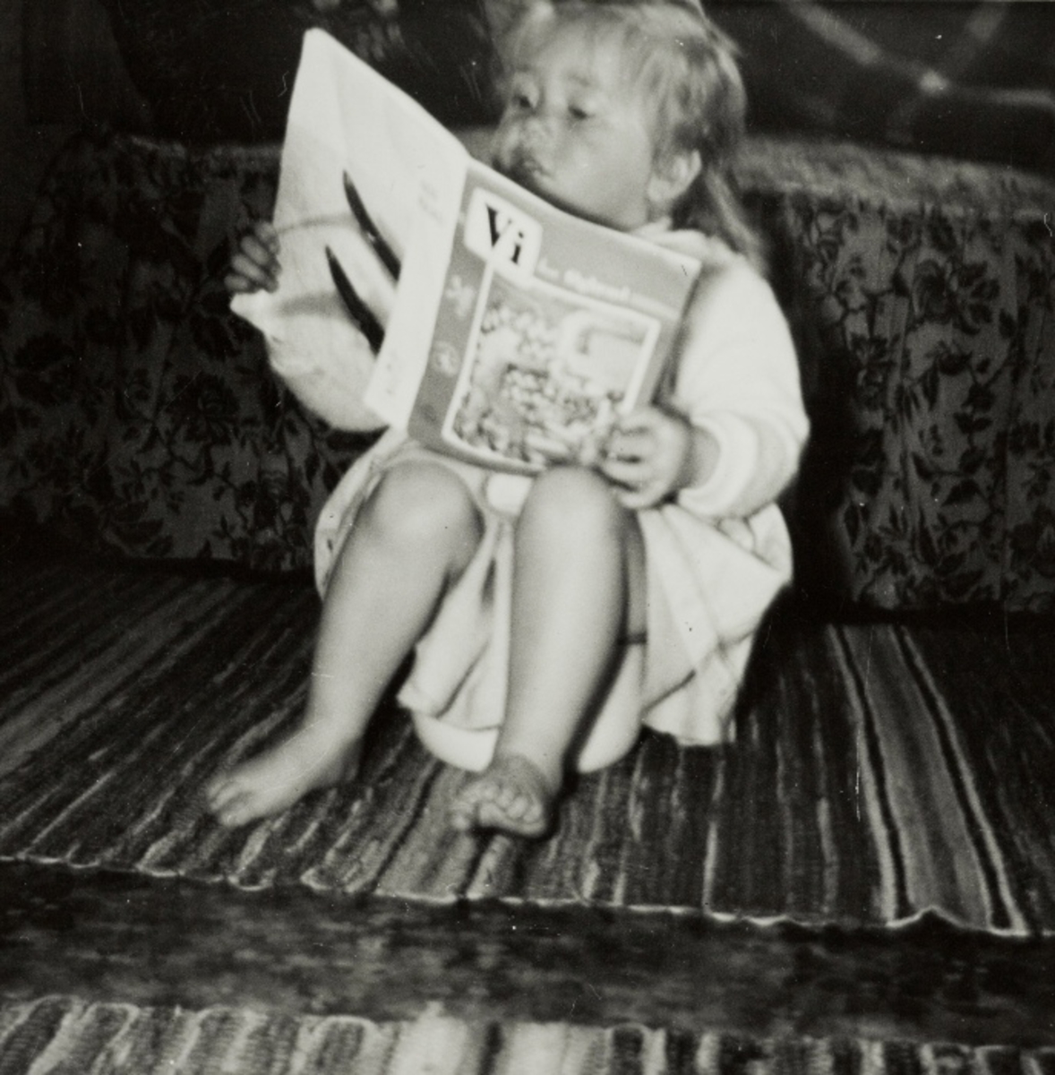 Ein liten jente sitter på gulvet og leser "Vi hos Øglænd"