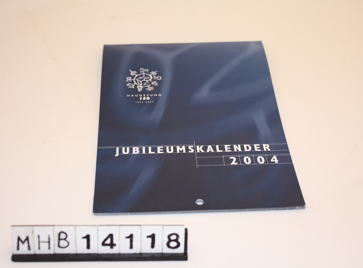 Kalender med rektangulær form og hull i nedre kortside til oppheng. Kalenderen er i hefte-format og inneholder en rekke bilder fra Haugesund.