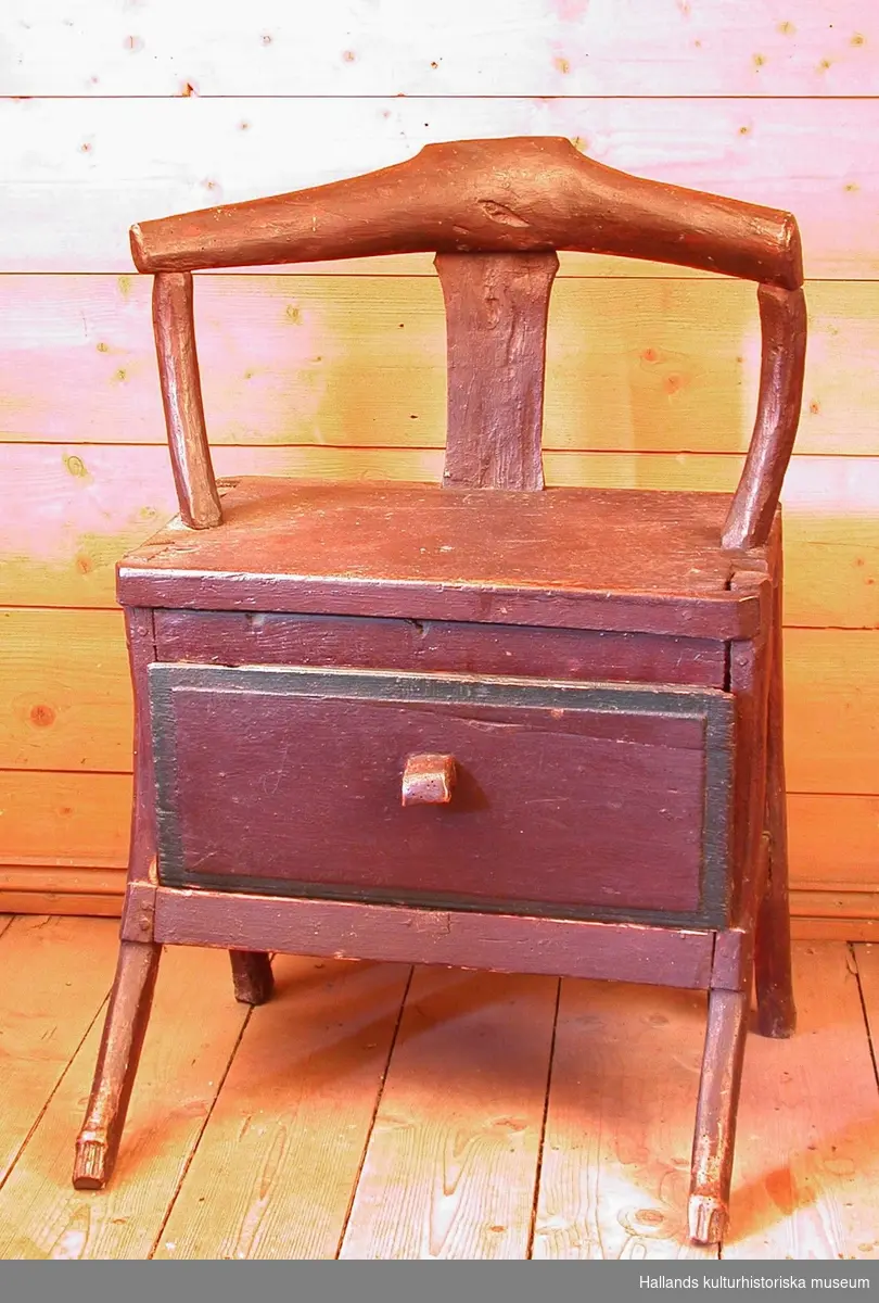Brunmålad trästol med låda med grön rand under sitsen.