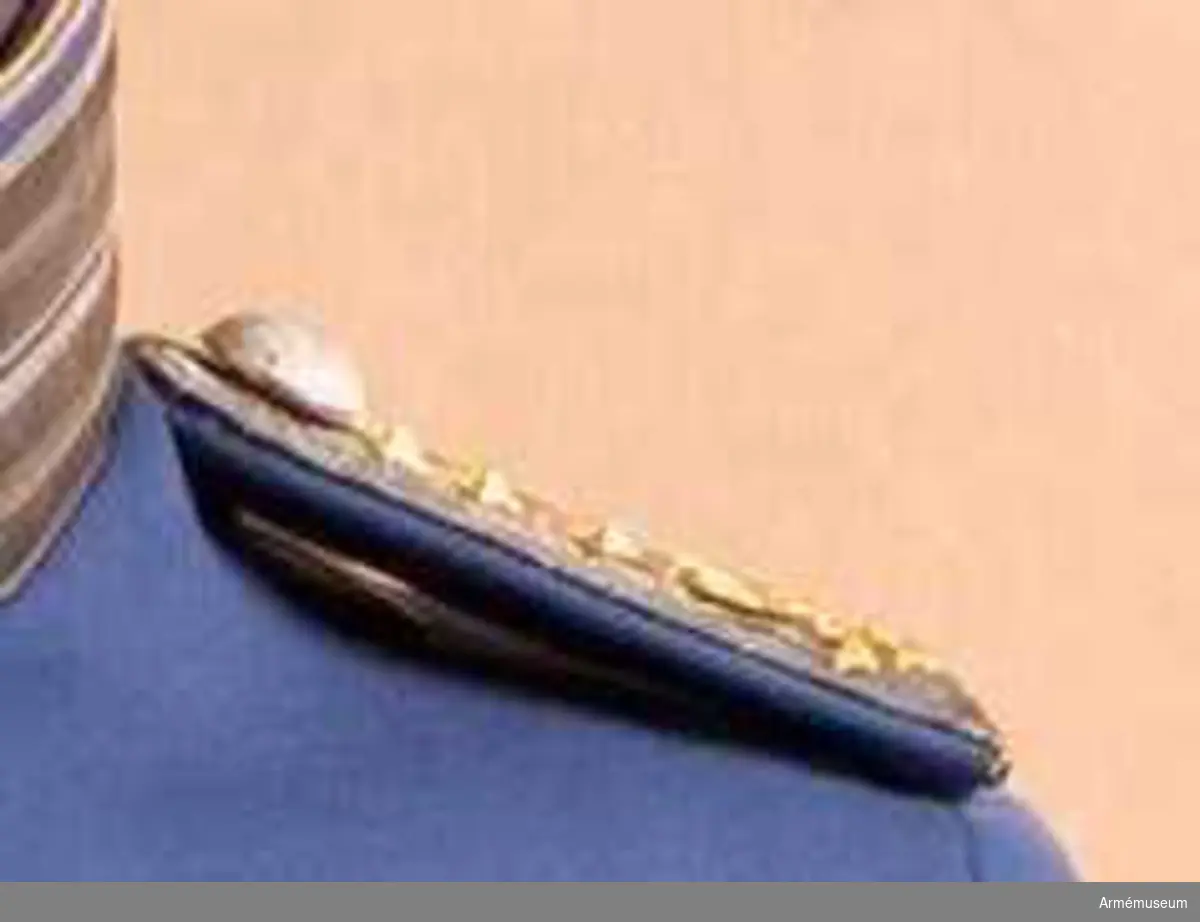 En styv matta överklädd med kläde i vapenrockens färg. Galon i silver lagd däröver i fem rader. Regementets knapp i silver (tre kronor) stora modellen. Tre guldstjärnor i rad (=ryttmästare). Tre små öppna kronor mot axelsömmen (ärmen). Över dessa en sluten krona i guld. På baksidan en mässingkrok märkt "Holts gulddrageri Stockholm" att fästas på vapenrockens axel. Tillsammans med ett band av kläde, fastsytt mot ytteraxel, bildar detta en stadig fast- sättning av axelklaffen.