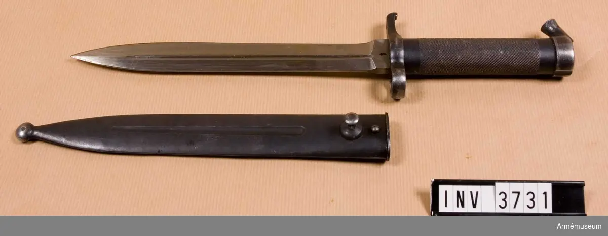 Knivbajonett m/1896 t gevär m/1896, m/1938/automatgevär m/1942.Består av: 1 bajonett, 1 balja av stål.Helt tillv. av stål med rörformigt lättrat grepp med konisk låsknapp och pipring. Rak, eneggad klinga med smal blodskåra på båda sidor. Klingb vid fästet: 25 mm. Pipringens id: 15,5 mm. Balja, l: 232 mm, vikt: 120 gr; tillv.nr 544.