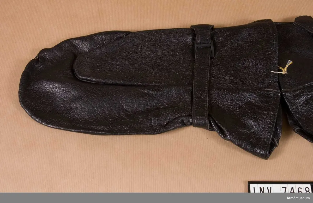 Handske fm/1958, ytter-.Tillverkad av svartbrunt skinn med åtdragaren på insidan av  handloven och med skinnhand upptill för att göra en ögla av att fästa runt armen. Färg svartbrun N.