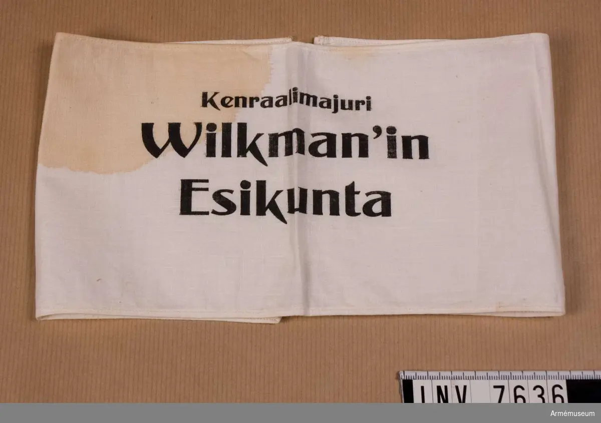 Armbindel, "Wilkman'in Esikunta". Finland.
Text: "Kenraalimajuri Wilkman'in Esikunta" det vill säga Generalmajor Wilkmans stab. Vit armbindel med svart tryck.Mått 450 x 125 mm, färg vit A.