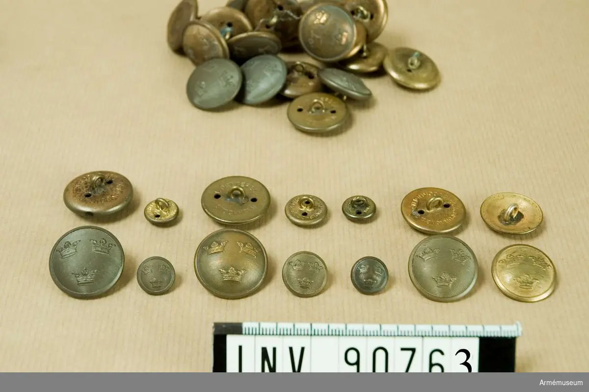 Låda märkt " I 1, I 2, I 3, I 4, I 5 m/1779 brons". Innehållande en stor mängd knappar små och stora. Ett kuvert märkt "sergeanter m/10, 23" ett annat märkt "m/04".