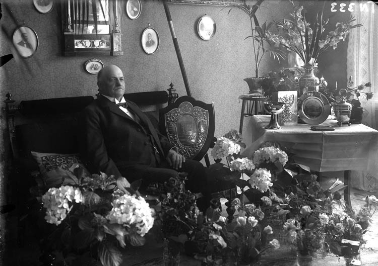 Enligt tidigare noteringar: "Fiskhandlare Karl Rasmusson i sitt hem, fotograferad med blommor och presenter vid högtidsdag."