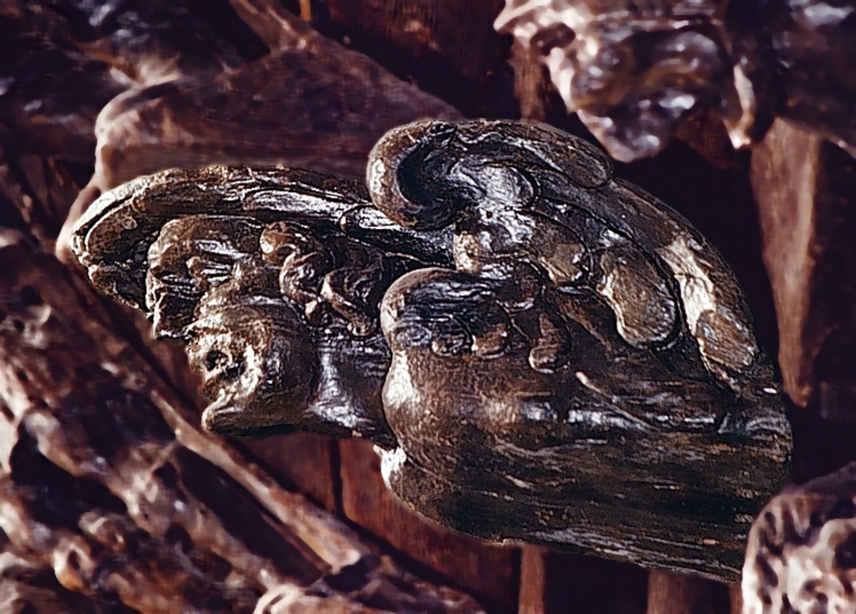 Skulpturen är formad som en konsol och återger ett mansliknande huvud och bröstparti.
Huvudet, med starkt förvridna anletsdrag, är kraftigt bakåtlutat. Vid axlarna sitter stora fågelvingar och på huvudet bär figuren en hårt vriden lagerkrans eller dylikt. Vid tinningarna ringlar sig tjocka hårlockar. Vinkeln mellan bak- och översidan markeras genom ett runt urtag.
Skulpturen är relativt välbevarad.

Text in English: Console carved as a male-like head and torso.
The features of the face on this head are twisted violently and the head leans backward at a sharp angle. There are large wings at the shoulders and the figure bears a tightly twisted laurel wreath on its head. There are thick curls of hair at the temples. The angle between the backside and topside is marked with a semi-round recess.
The sculpture is rather well preserved.