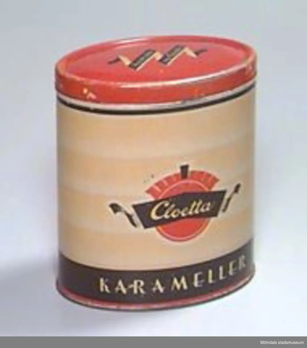 Oval hög burk med lock. Målat i svart, rött och gult: "Tag det rätta, tag Cloetta" på locket, "Cloetta karameller" på sidorna.