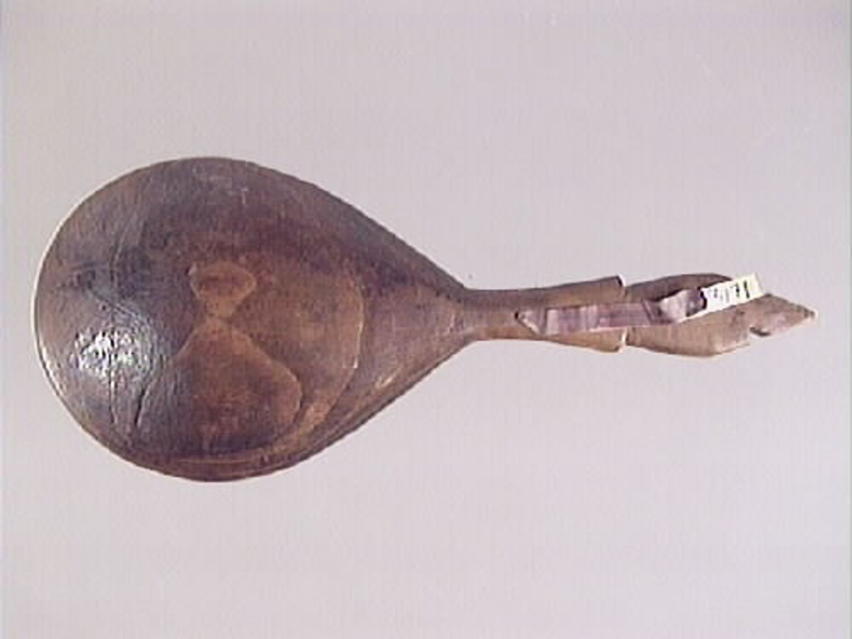 En träsked.
Skeden har ett ovalt skedblad och ett kort skaft. Skaftet är profilerat i tre avsatser. Skaftets ände är formad till en spets. På skeden syns spår av färg.
Skeden är mycket välbevarad, bortsett från en liten spricka som är synlig på baksidan.

Text in English: Wooden spoon with egg-shaped bowl and short, profiled handle ending in a point.
Intact and well preserved except for a small crack on the reverse.