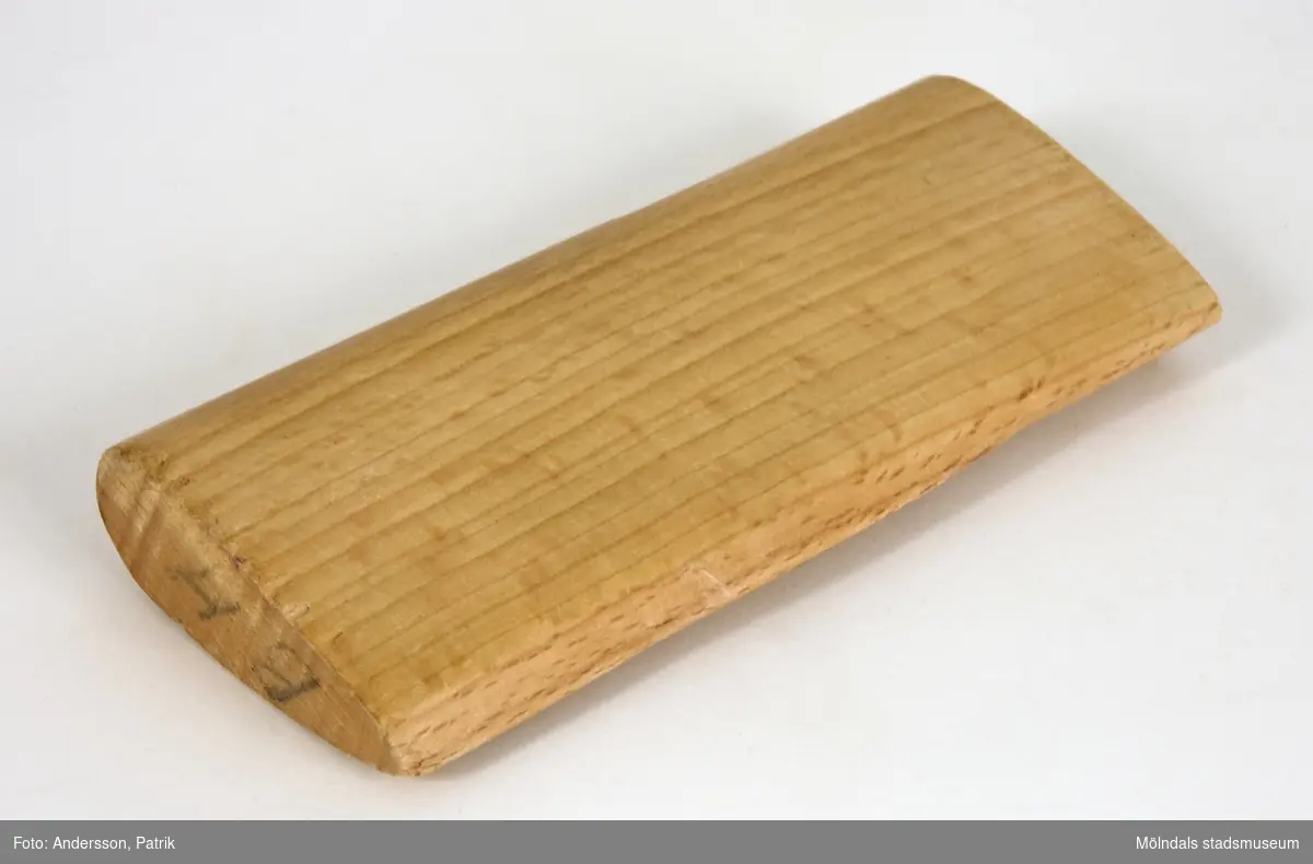 Träverktyg, troligen tyngd, som har använts vid papperstillverkningen på Papyrus. Verktyget är droppformat i genomskärning, och är märkt med initialerna "BH". 
