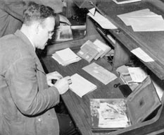 Värdebrevbärare vid postkontoret Stockholm 1, 1940 - 1942. Till
höger synes blecklåda med penningar, postanvisningar och
giroutbetalningskort. Mars 1942.