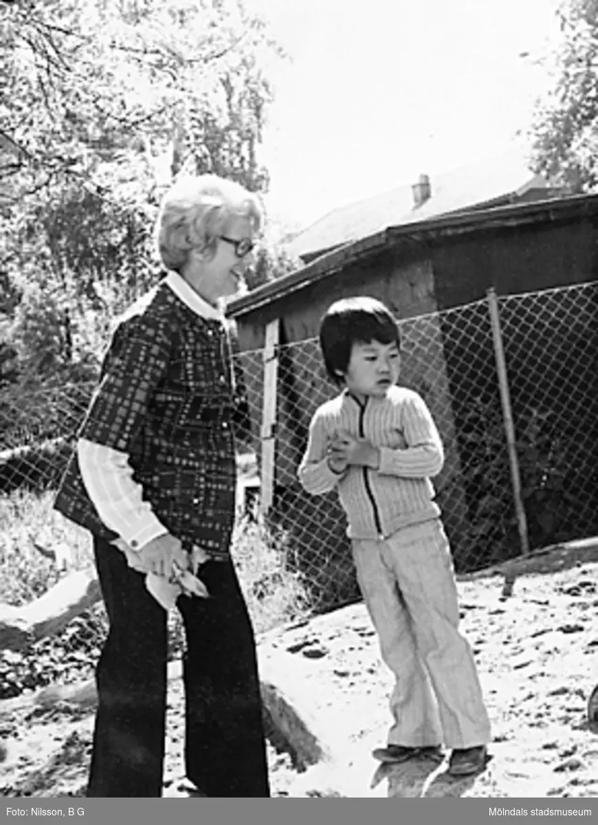 En lärarinna och ett dagbarn som står ute på lekplatsen vid Holtermanska daghemmet juni 1973.