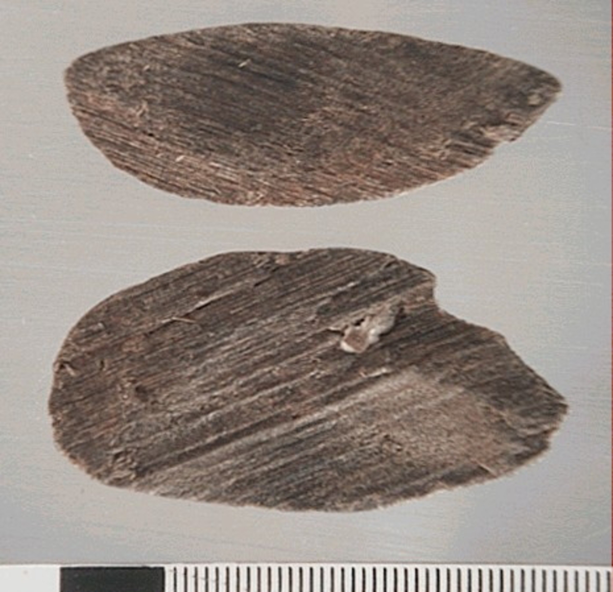 Två delar av en träsked. Delarna utgör mindre partier av skedbladet. På delarna syns en svagt rödbrun färg, vilket möjligen är spår efter bemålning.
Delarna är mycket slitna.