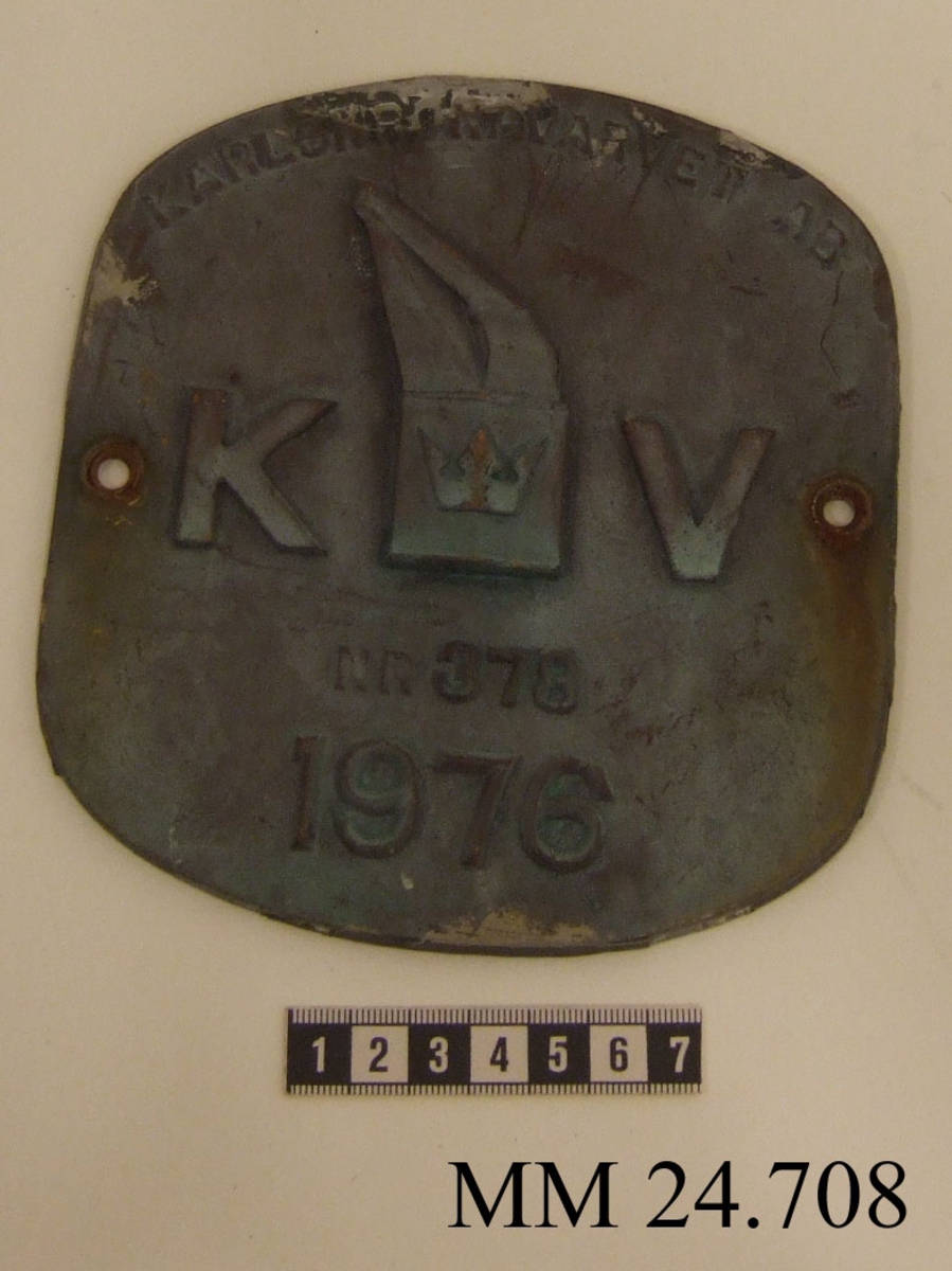 Metallskylt med inskription i relief. Texten på skylten lyder: Karlskronavarvet AB KV NR 378 1976. I mitten, dvs. texten KV, utformad som Karlskronavarvets logotype. Hål borrat i varje långsida.