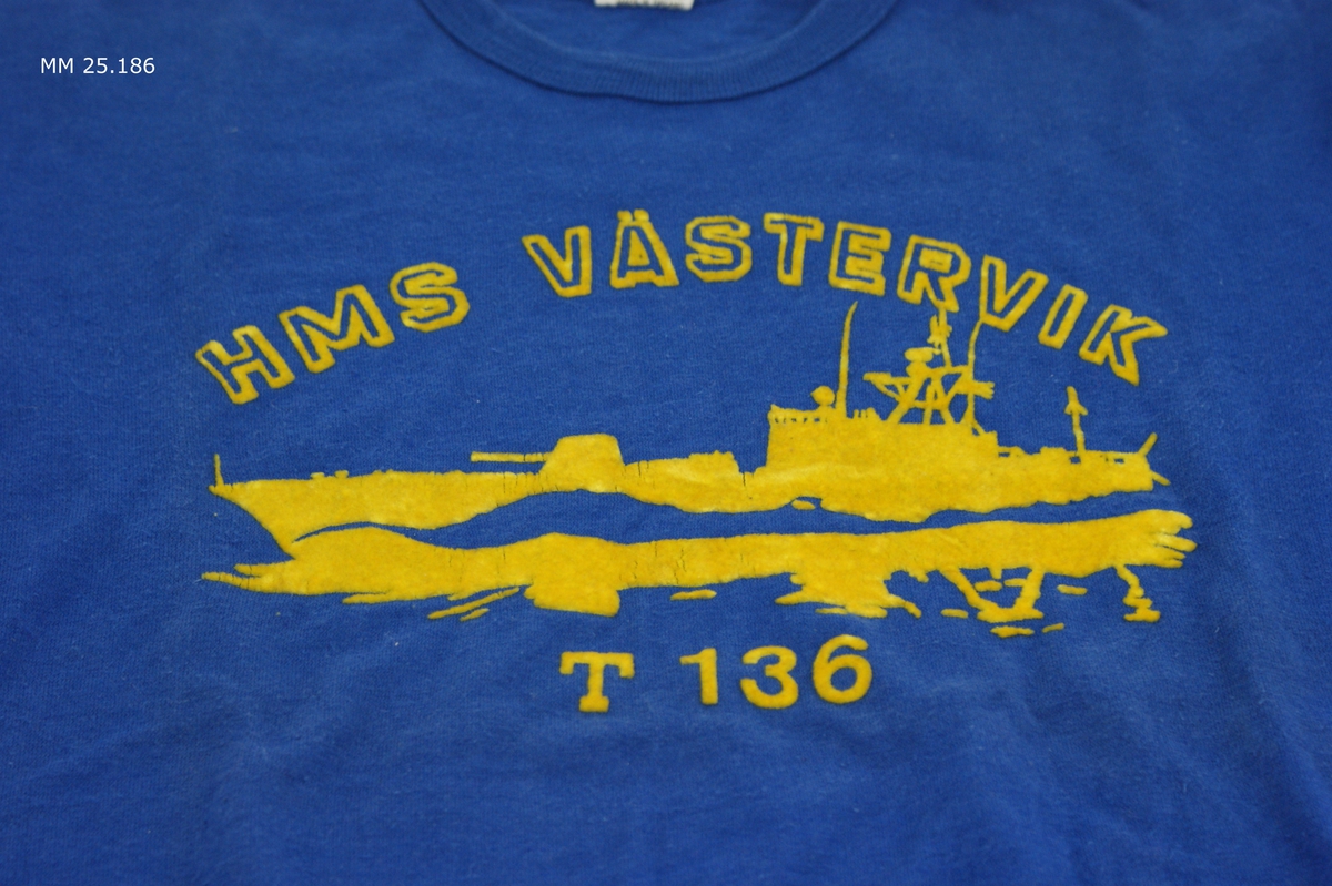 Marinblå kortärmad t-shirt med gult tryck i plyschaktigt material. Text: "HMS Västervik T 136" och en torpedbåt till sjöss.