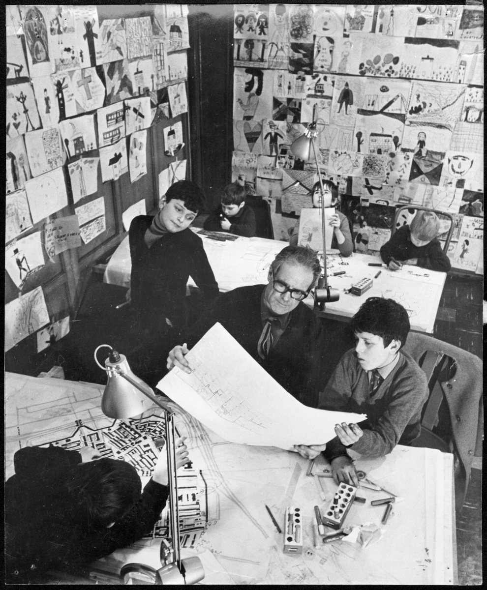 Byker
Interiör av ritningsateljén i Byker. Erskine sitter, omgiven av barn, vid ett ritbord.