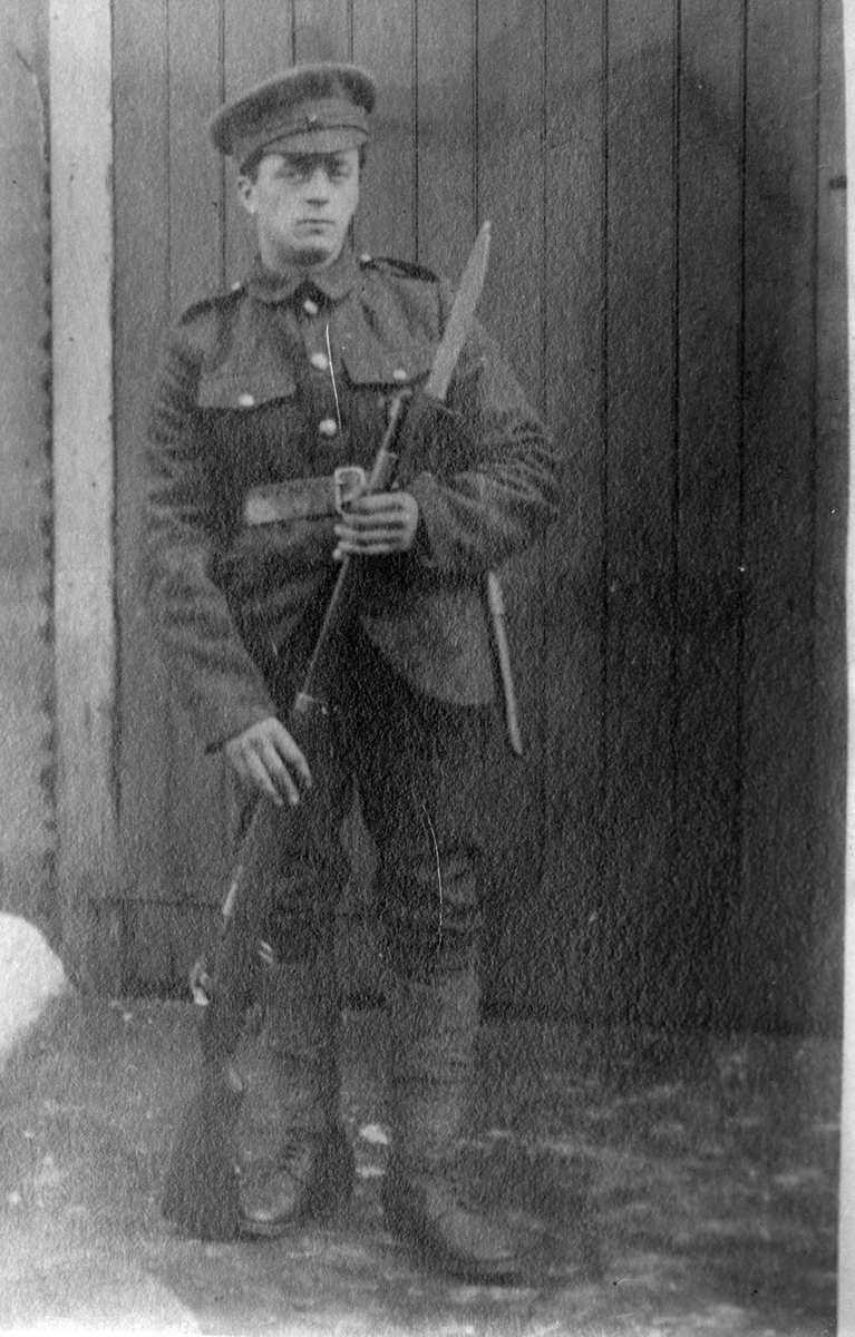 Britisk soldat fotografert foran en vegg med gevær og bajonett. Bildet er neppe tatt av Magdalene Norman, men er reprodusert av henne.