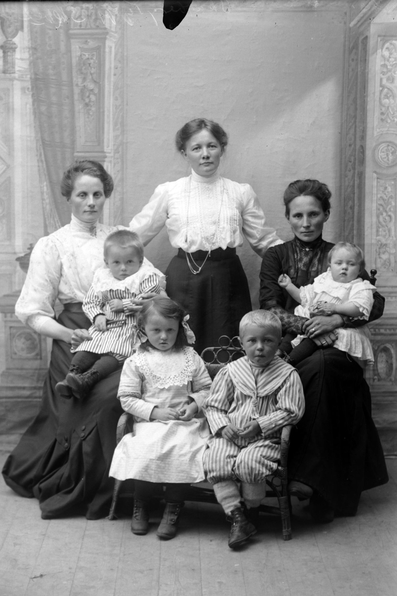 Studioportrett av tre kvinner med fire barn foran seg.