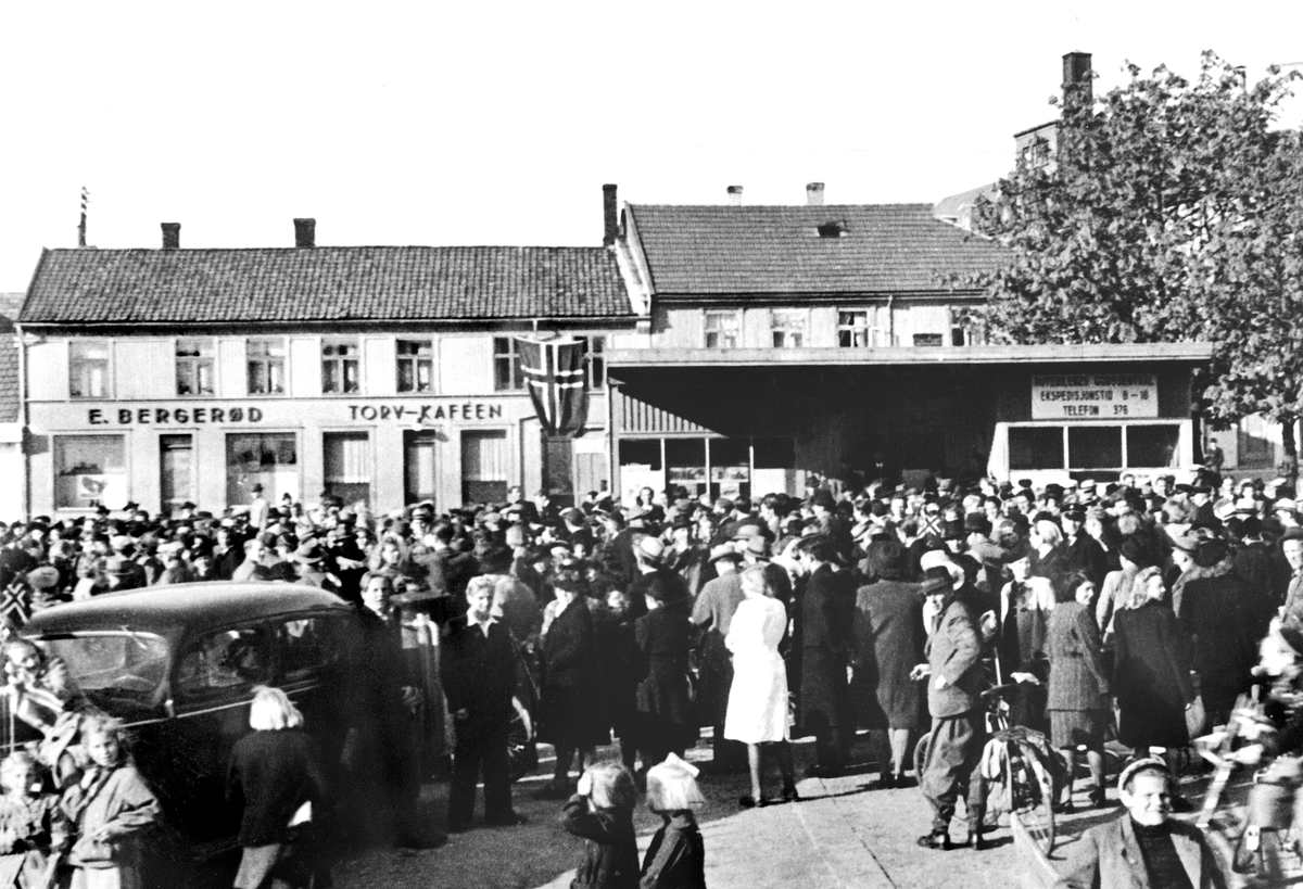 Da freden "brøt løs" i maidagene 1945. Fra Torvet i Sarpsborg.
Rutebilenes godssentral til høyre,  og skilt for E. Bergerød og Torvkafeen.