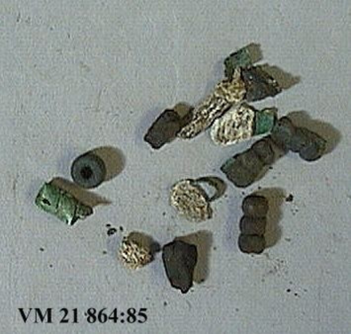 Fyra glaspärlor. Delvis brandskadade. Tre av pärlorna består var och en av tre sammansatta pärlor.

Mått: 1,5 x 0,7 cm. - 0,9 x 0,7 cm.

Bronsspiral från vilken ett antal fragment fallit. Mått: L. 1,4 cm. Diam. 0,6 cm.

Två kolbitar. Mått: 1,3 x 1 cm. - 1 x 0,6 cm.

Fem fragment av bränt ben. Mått: 1,7 x 0,6 cm. - 0,9 x 0,8 cm.

En keramikskärva. Mått: 1 x 0,8 cm.



Omärkta fynd men placerade i särskild ask bland keramik VM 21 864:83