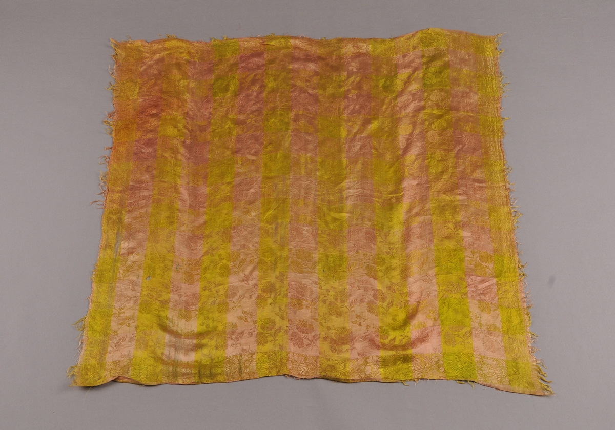 Tørkle av silkedamask med gulgrønne og gamalrosa striper som dannar eit rutemønster langs kantane. Heile tørkleet er jamnt blomstrete over heile. Korte frynser.
