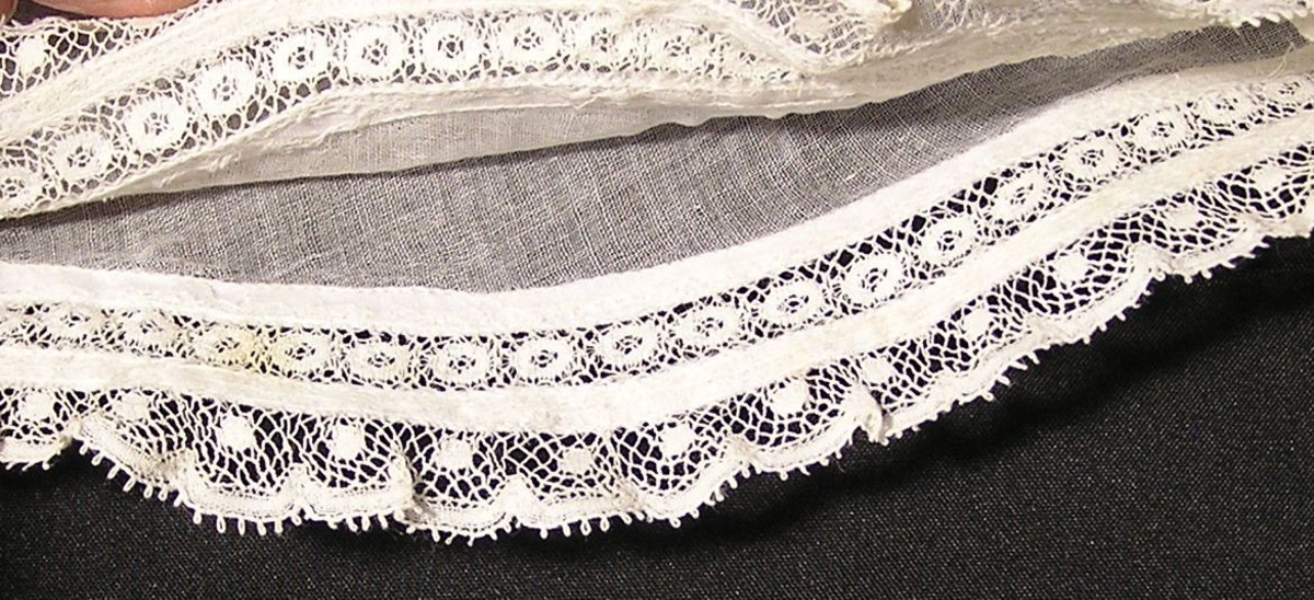 Maskinblonde påsydd med 1-tråds symaskin. Øvre del en søm. Ttilsydd mansjett, rynket på oversiden.