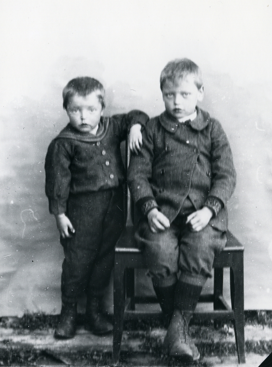 To gutter fotografert med lerretbakgrunn, den ene sittende på stol