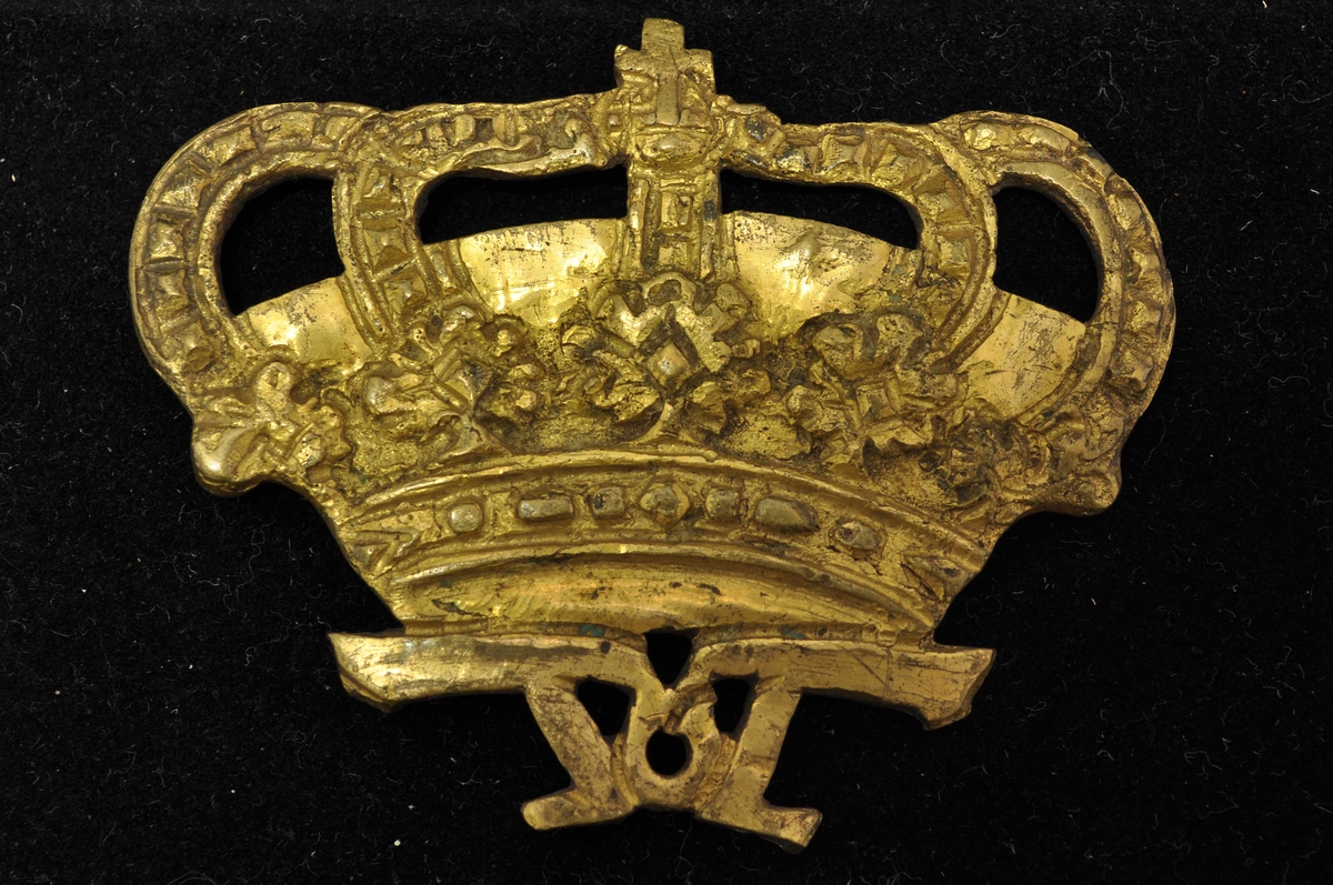 Krone med kors på toppen, rester av nål og feste på baksiden.