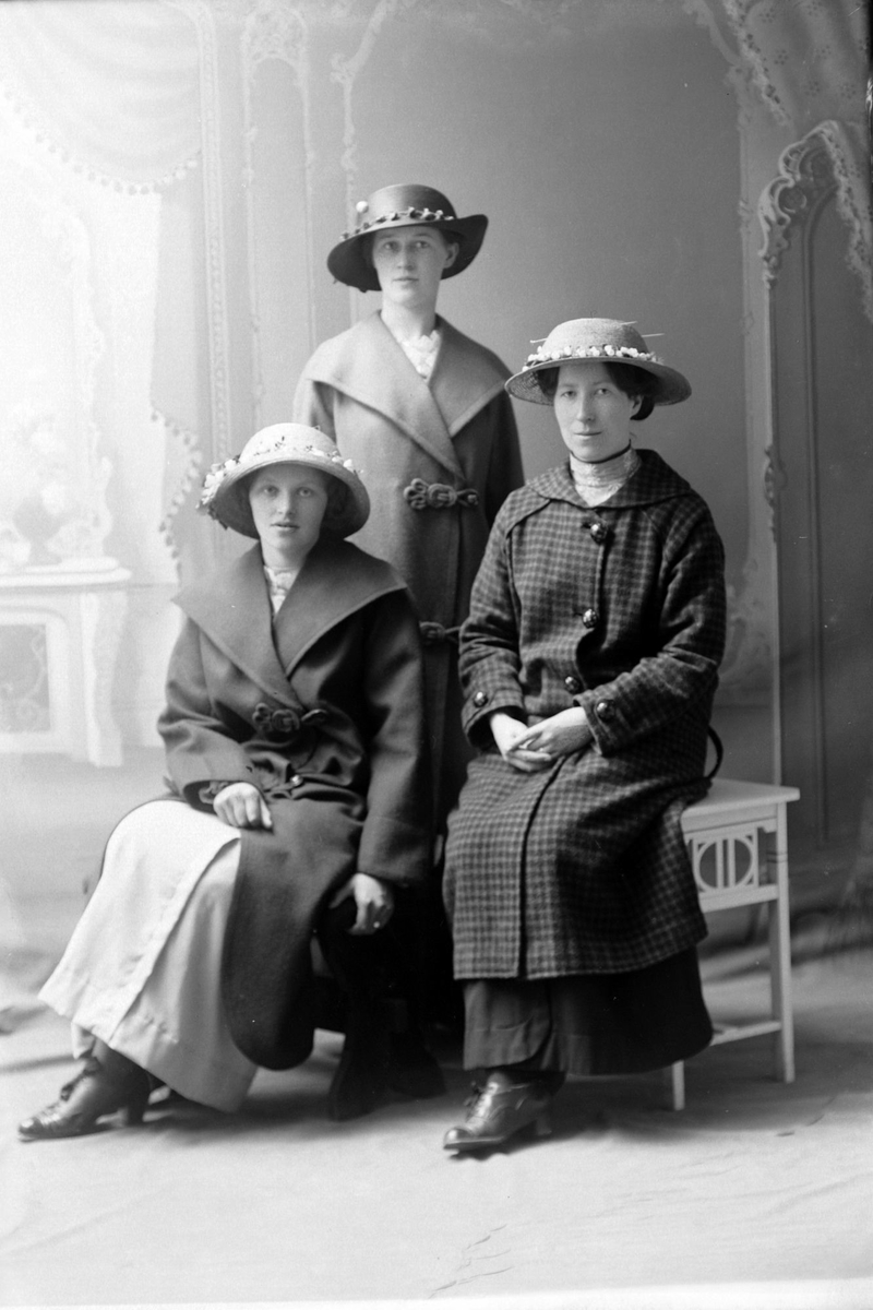 Studioportrett i helfigur av tre kvinner, alle med hatter på hodet.
