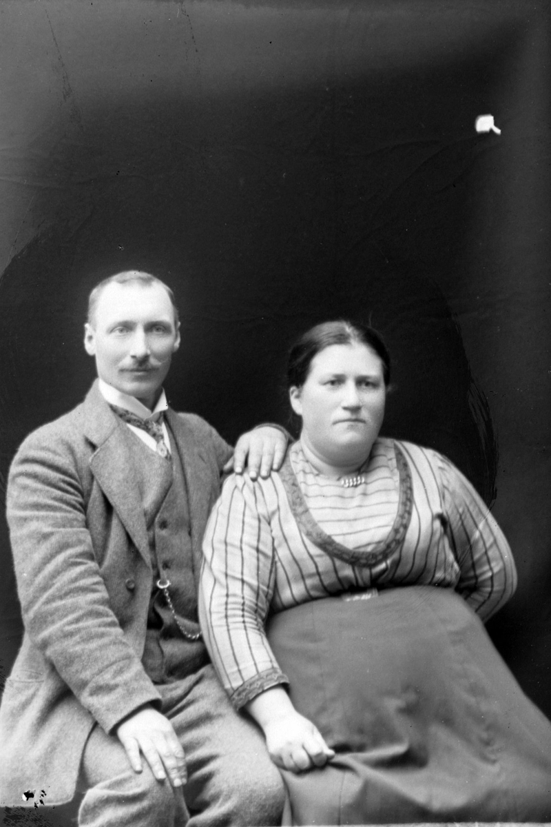 Studioportrett av en mann og kvinne som sitter foran en mørk bakgrunn.