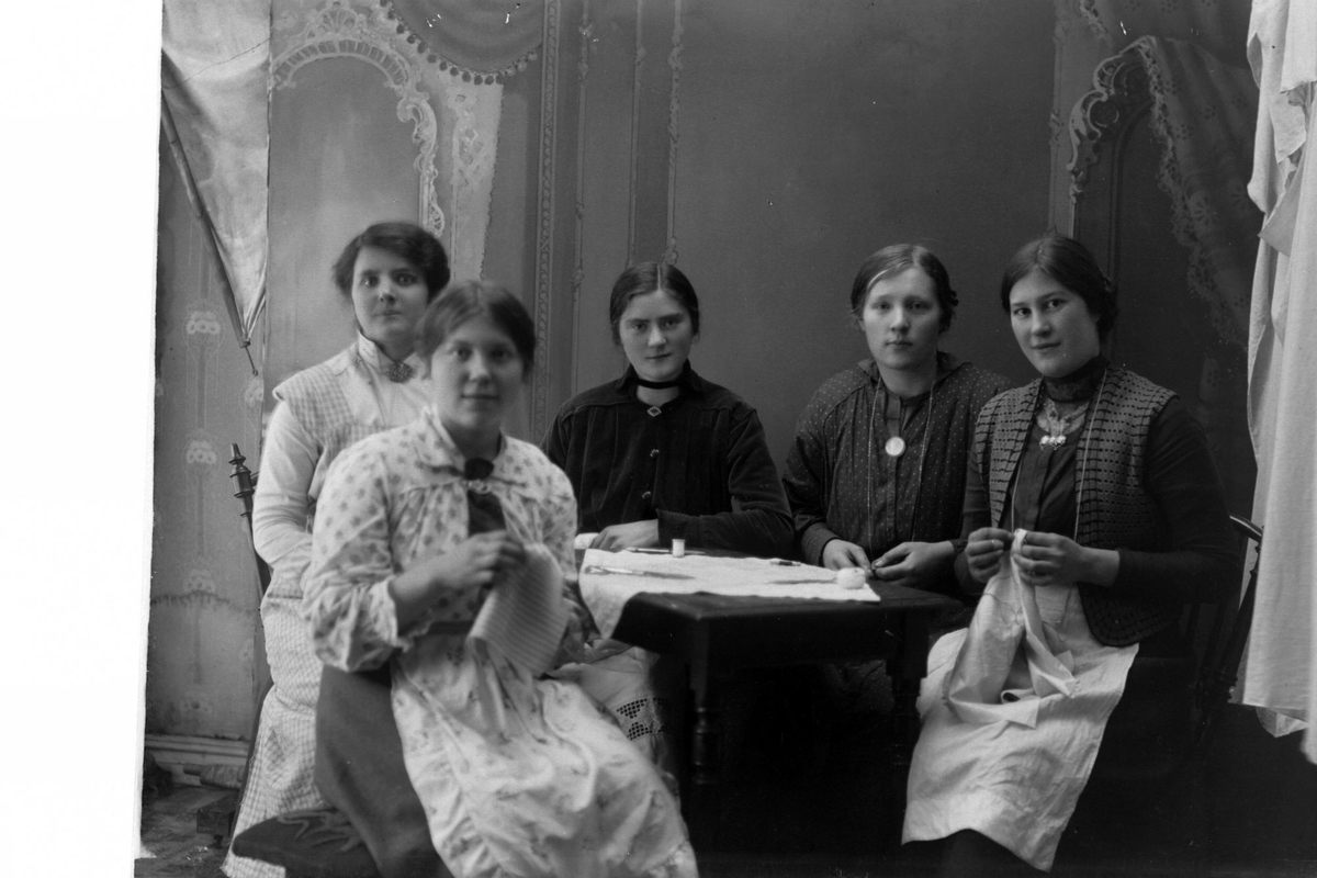 Studioportrett av fem kvinner ved et bord med sysaker på.