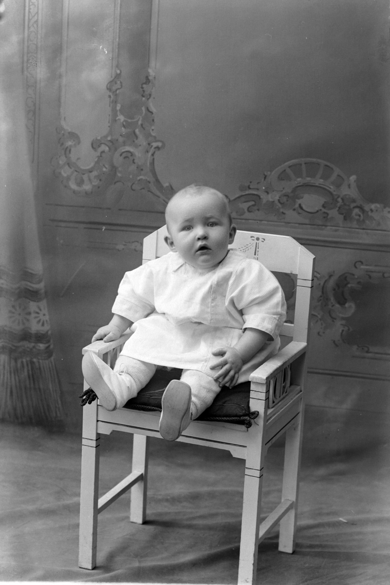 Studioportrett av et spedbarn i en stol.